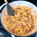 Sauerkraut Sausage Skillet meal being stirred with wooden spoon in a cast iron pan.