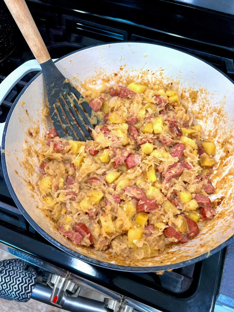 Sauerkraut Sausage Skillet meal being stirred with wooden spoon in a cast iron pan.